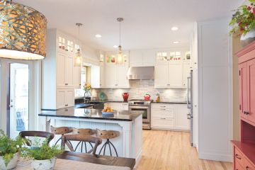 Bright white kitchen with island, pendant lights, stainless steel appliances, and dining table in a modern home
